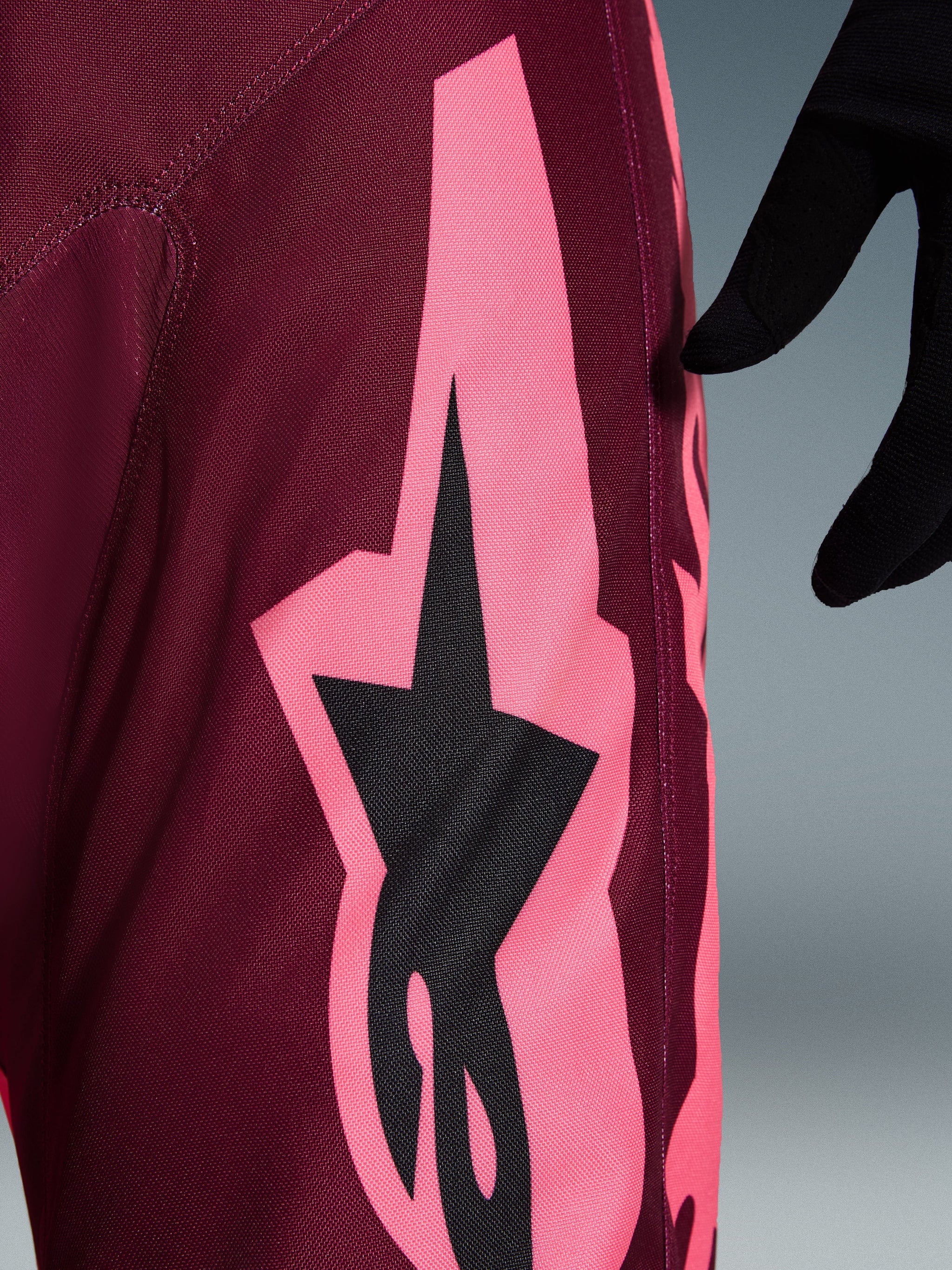Alpinestars 2026 Racer Riway Hose, Motocross-Hose, Dark Red Coral, Nahaufnahme mit einer großen korallenrosa kantigen Grafik und schwarzem Stern-Logo, hebt die strapazierfähige Poly-Gewebe-Textur und die Performance-Nähte hervor