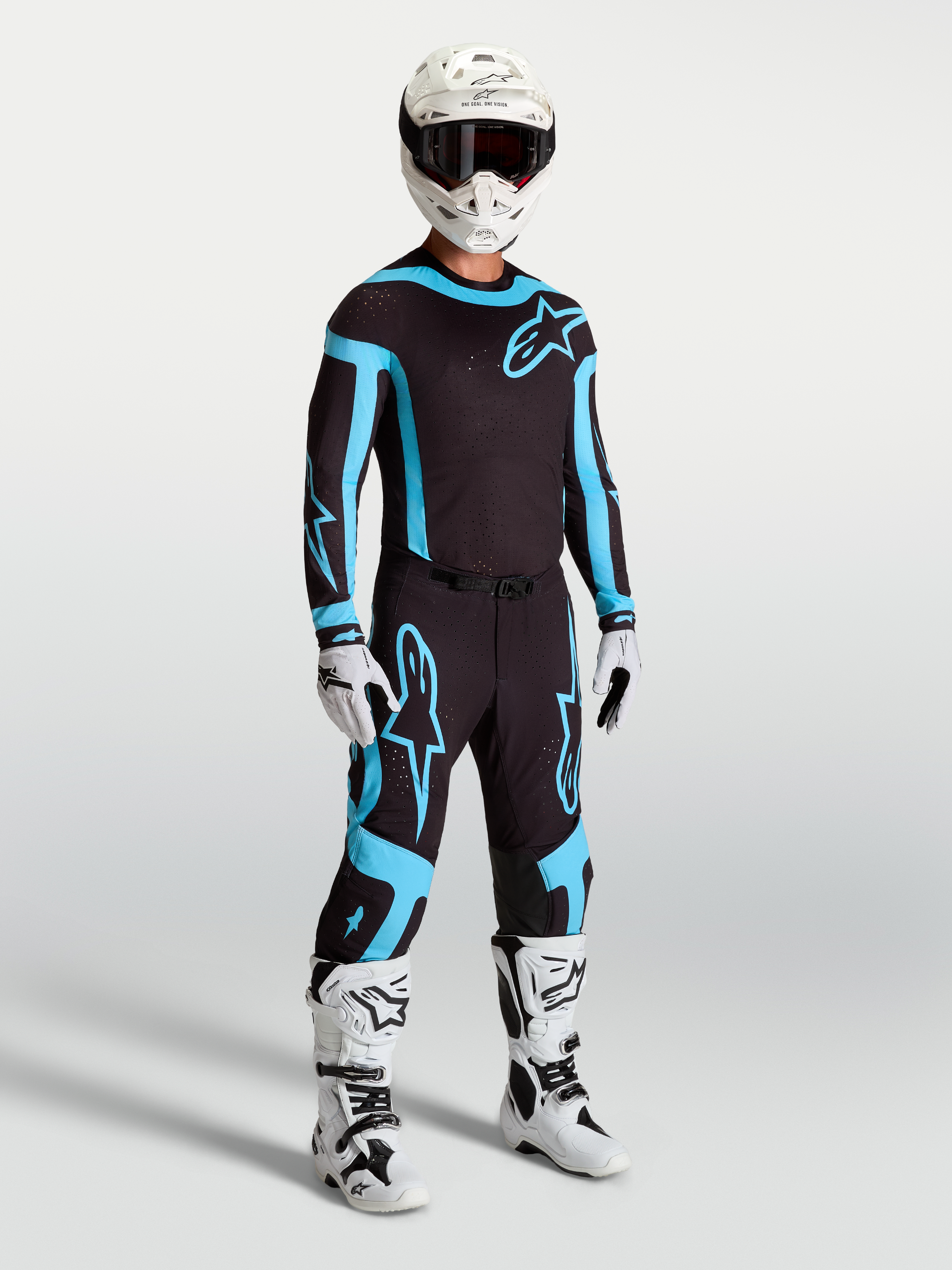Alpinestars Supertech Vesta Hose, Motocross-Rennbekleidung für Herren in Schwarz und Türkis mit weißen Stiefeln und Helm.