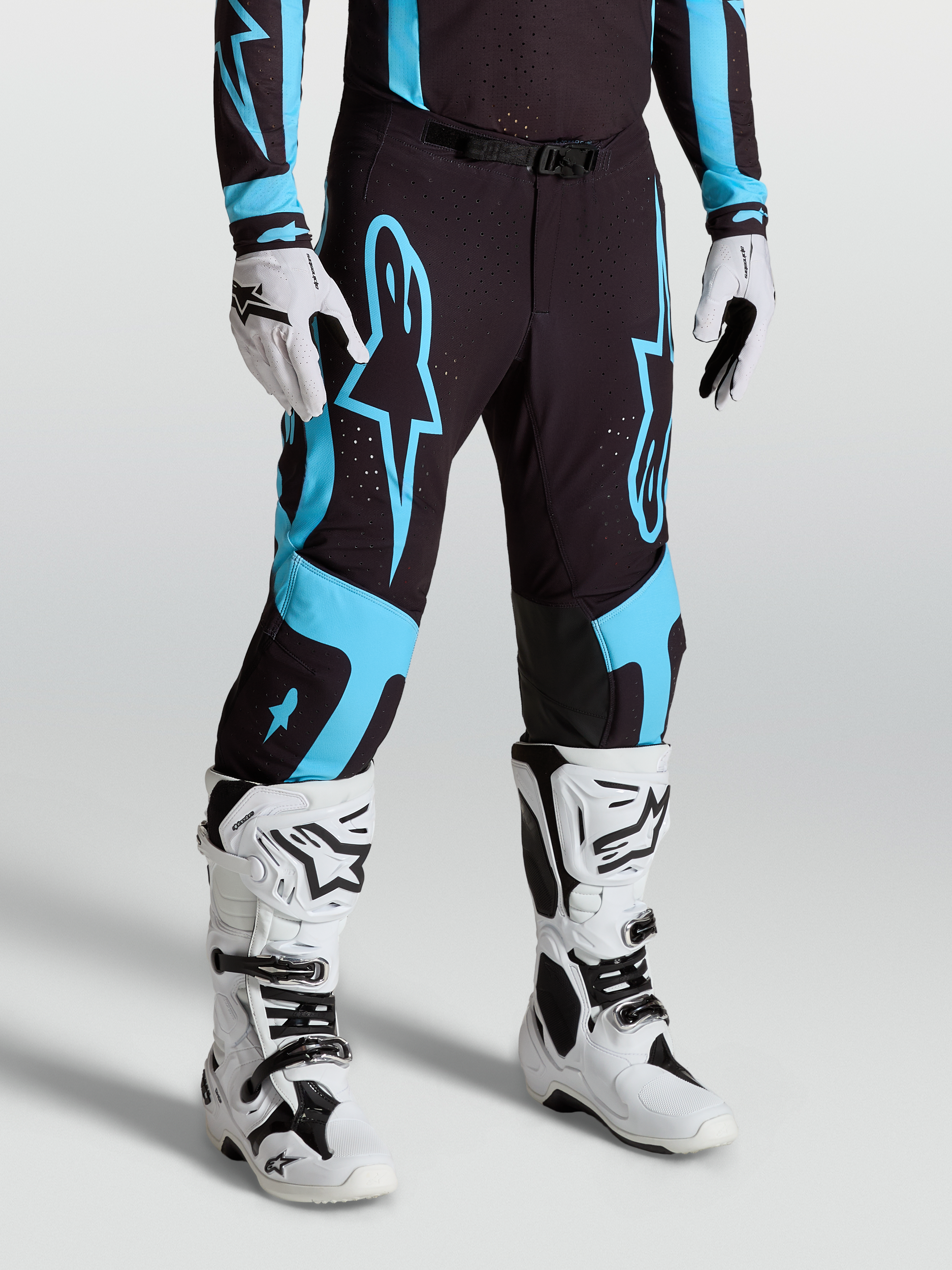 Alpinestars Supertech Vesta Hose, Motocross-Rennsport-Hose für Herren, Schwarz und Türkis, aus Stretch-Ripstop mit Innenkniepanels aus Ziegenleder, getragen mit weißen Tech 10 Stiefeln und Handschuhen.