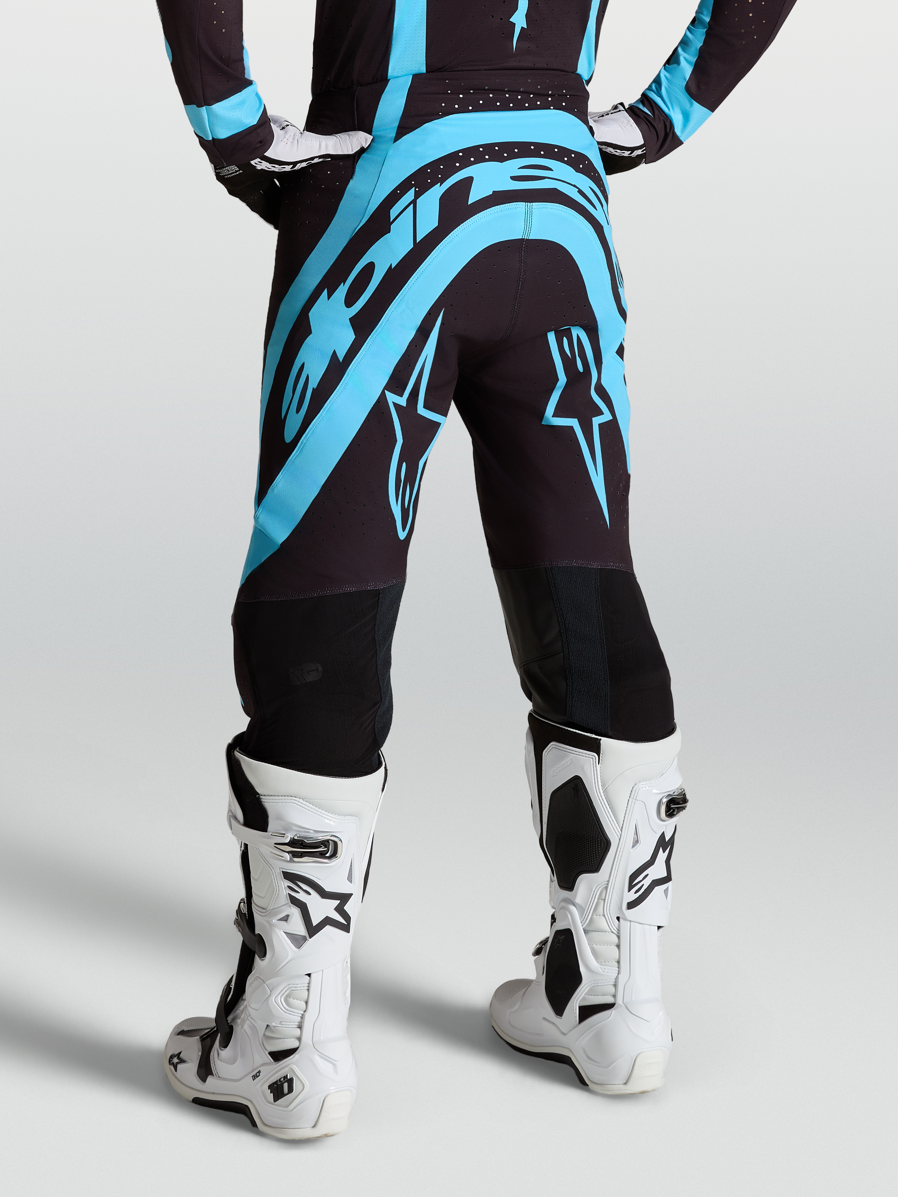 Alpinestars Supertech Vesta Hose, Motocross-Ausrüstung in Schwarz und Türkis, Rückansicht am Model mit weißen Rennstiefeln