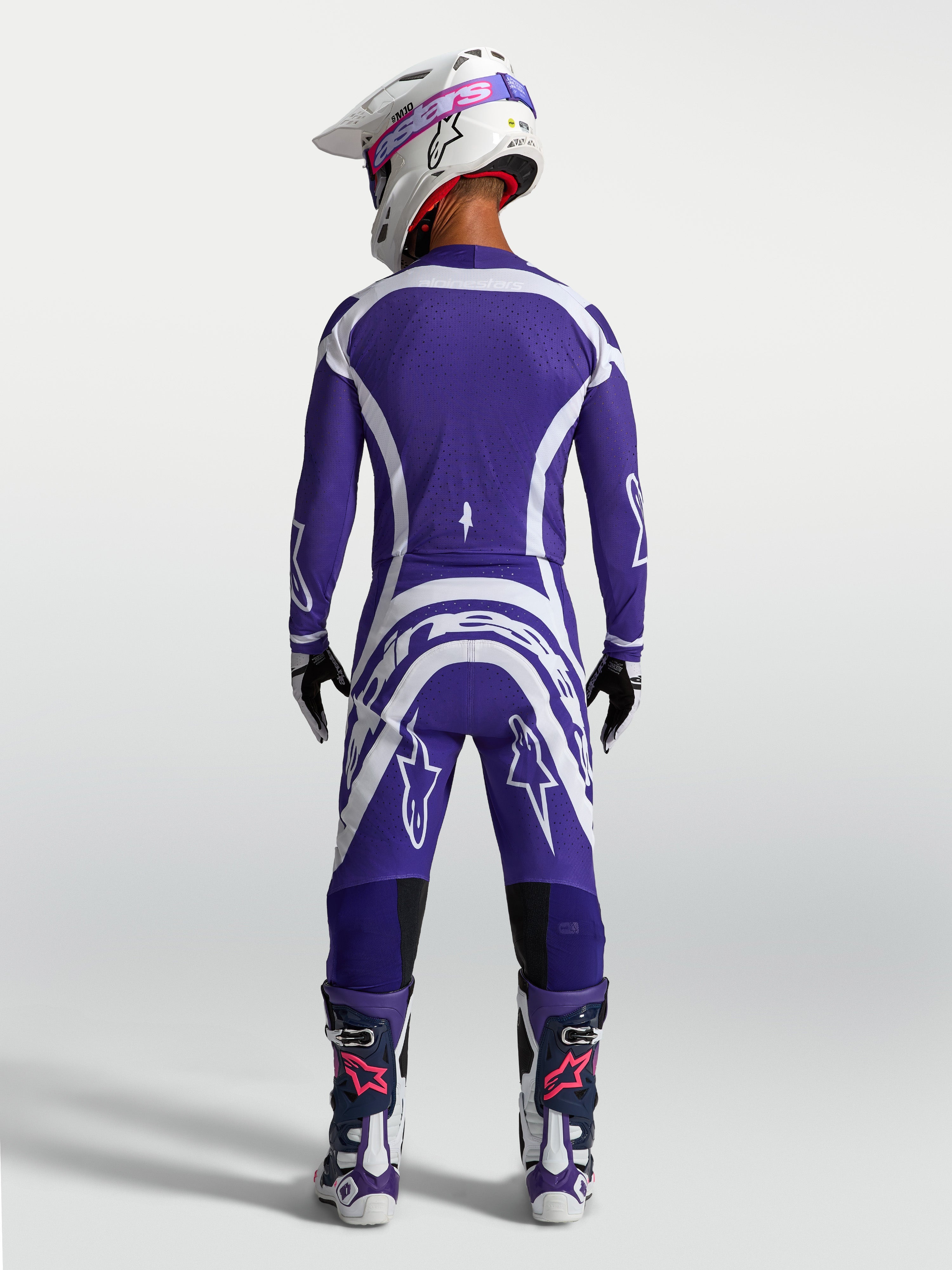 Alpinestars Supertech Vesta Trikot und Hose, Motocross-Rennausrüstung in Blau und Weiß, Rückansicht am Model mit Helm und Stiefeln.