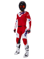 Alpinestars 2025 Racer Veil Hose, Motocross-Hose, Hellrot und Weiß, getragen als Teil einer kompletten Rennausrüstung mit passendem rot-weißen Trikot, schwarzem Helm mit oranger Brille, weißen Stiefeln und roten Handschuhen, mit auffälligen blauen Alpinestars-Logos.