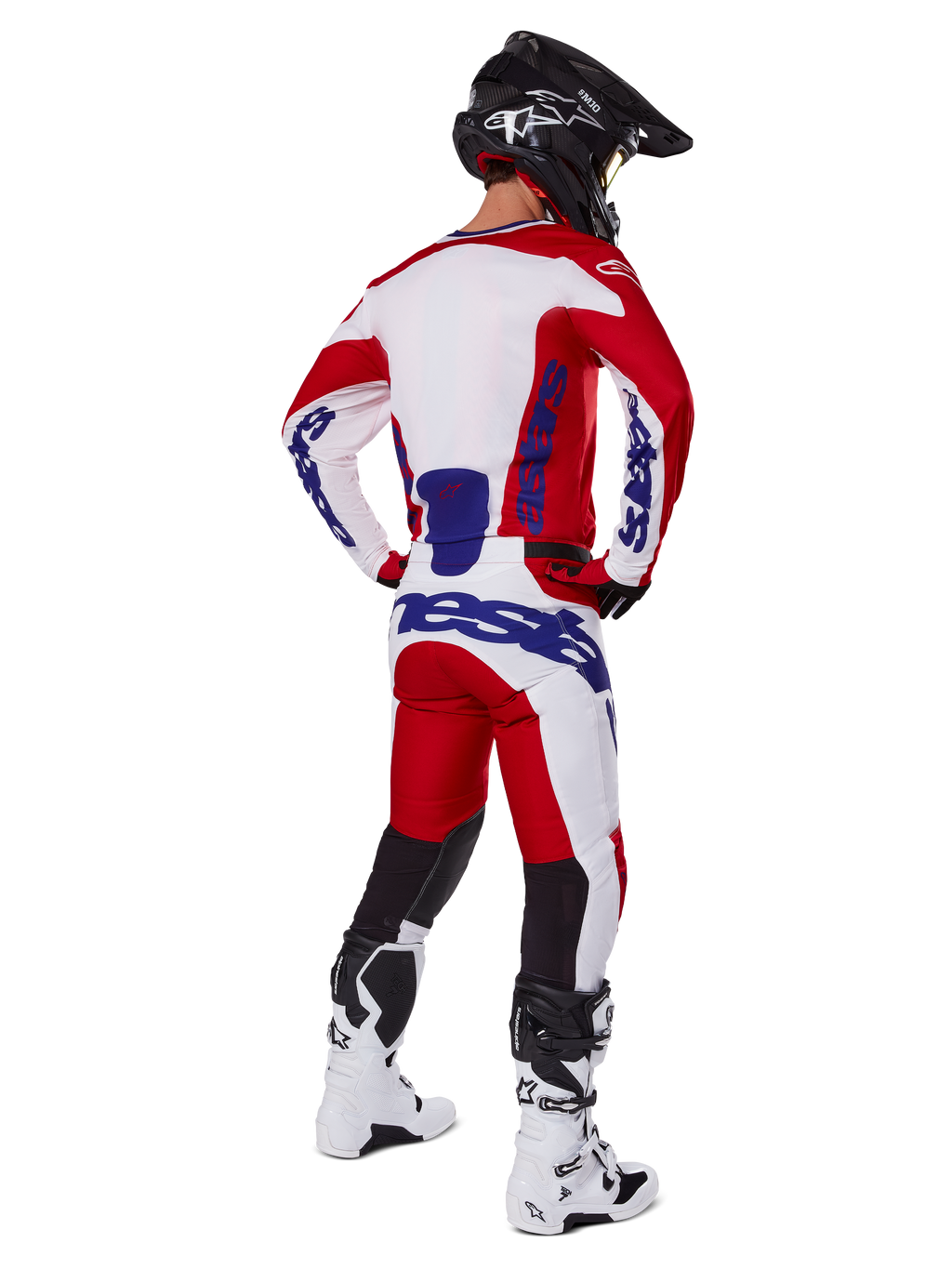 Alpinestars 2025 Racer Veil Hose, Motocross-Hose, Hellrot und Weiß mit blauen Akzenten, Rückansicht eines Fahrers in kompletter Ausrüstung, markantes Alpinestars-Branding, atmungsaktive Einsätze an den Unterschenkeln, dazu passende weiße Stiefel und schwarzer Helm.