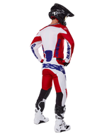 Alpinestars 2025 Racer Veil Hose, Motocross-Hose, Hellrot und Weiß mit blauen Akzenten, Rückansicht eines Fahrers in kompletter Ausrüstung, markantes Alpinestars-Branding, atmungsaktive Einsätze an den Unterschenkeln, dazu passende weiße Stiefel und schwarzer Helm.