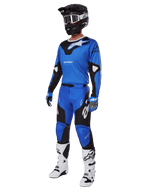 Motocross-Fahrer in kompletter Rennausrüstung, mit Alpinestars Racer Veil Hose 2025 in Blau und Schwarz, passendem blauen Trikot mit weißen Akzenten, schwarzem Helm mit weißer Schutzbrille, weiß-schwarzen Stiefeln und blauen Handschuhen, abgestimmtes Outfit für Offroad-Rennen