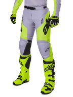 Alpinestars 2025 Racer Veil Hose, Motocross-Hose, Grau und Neongelb Fluo, mit schwarzen Stern-Logos und verstellbarem Hüftgurt, abgebildet mit passenden Motocross-Stiefeln und Handschuhen, ergonomisches Design für den Offroad-Einsatz
