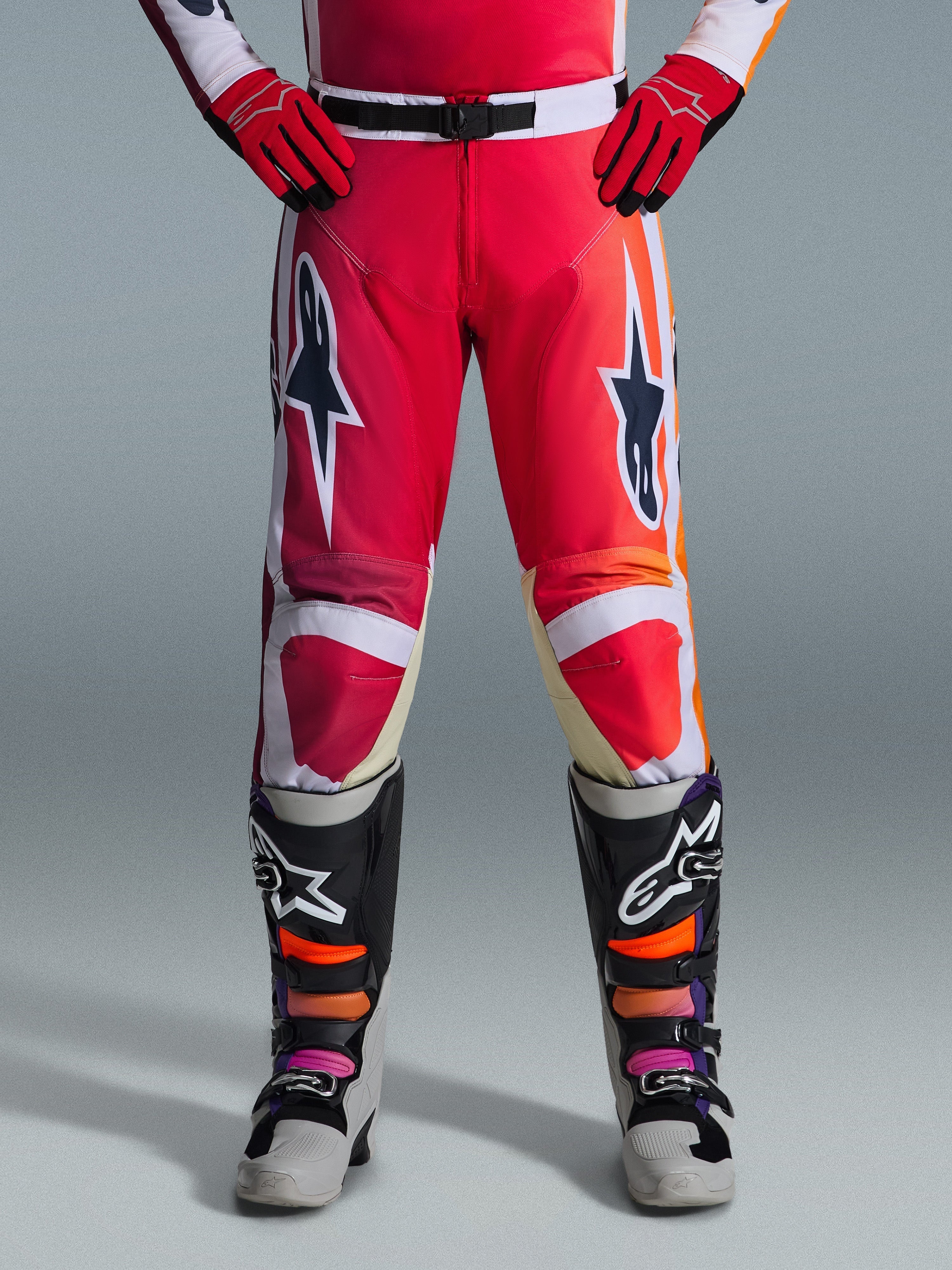 Alpinestars 2026 Racer Portl Hose, Motocross-Hose, Rot, Hellgrau und Dunkelgrau, getragen mit passenden roten Handschuhen und mehrfarbigen Stiefeln, mit markanten Alpinestars-Sternlogos auf den Oberschenkeln und weißen Akzenten, sportliches Design für Offroad-Rennsport