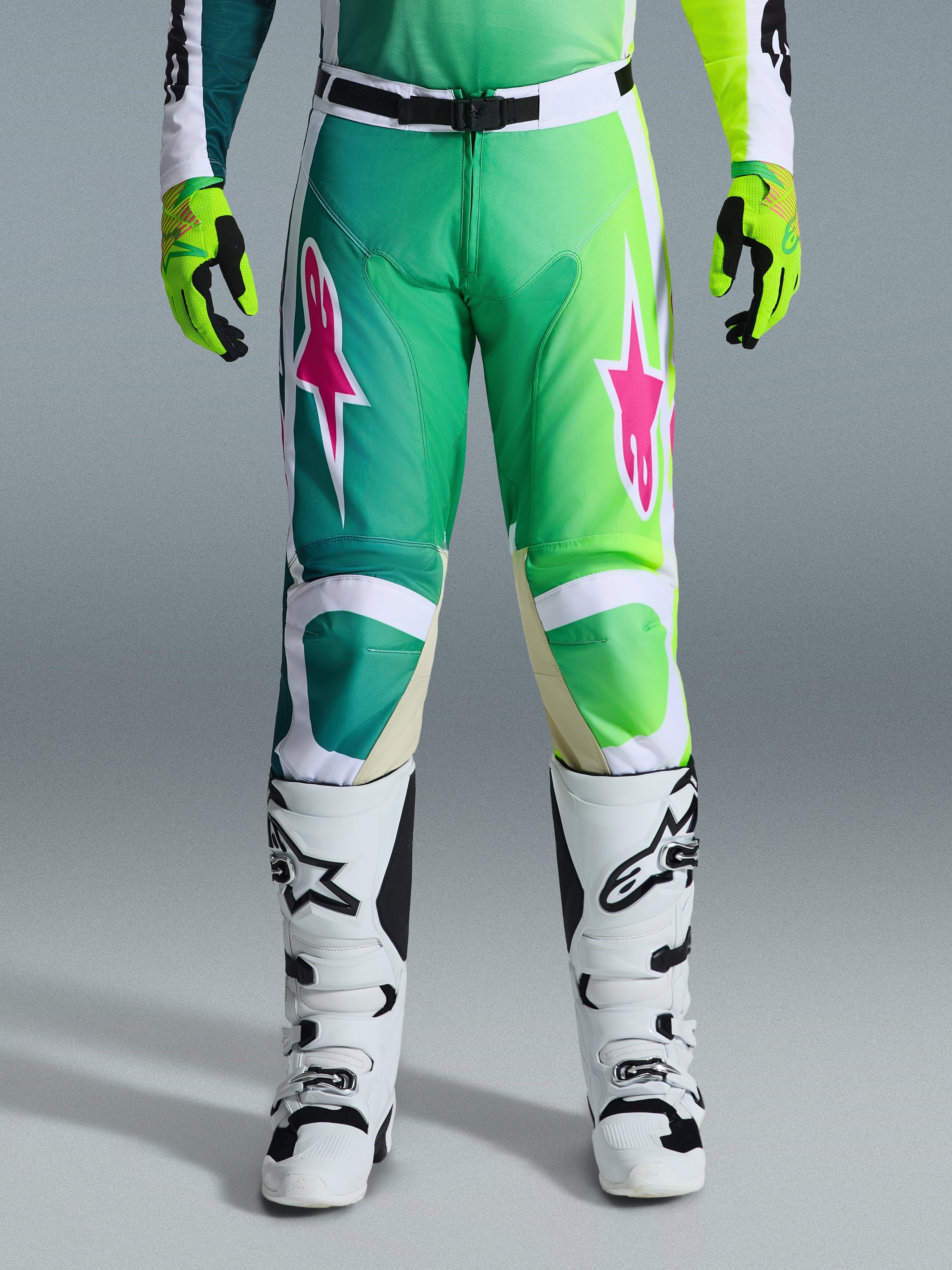 Alpinestars 2026 Racer Portl Hose, Motocross-Hose, Grün, Weiß und Schwarz mit pinkfarbenen Stern-Logos, kombiniert mit weiß-schwarzen Stiefeln und limettengrünen Handschuhen, Farbverlauf-Design und ergonomische Passform für den Offroad-Rennsport