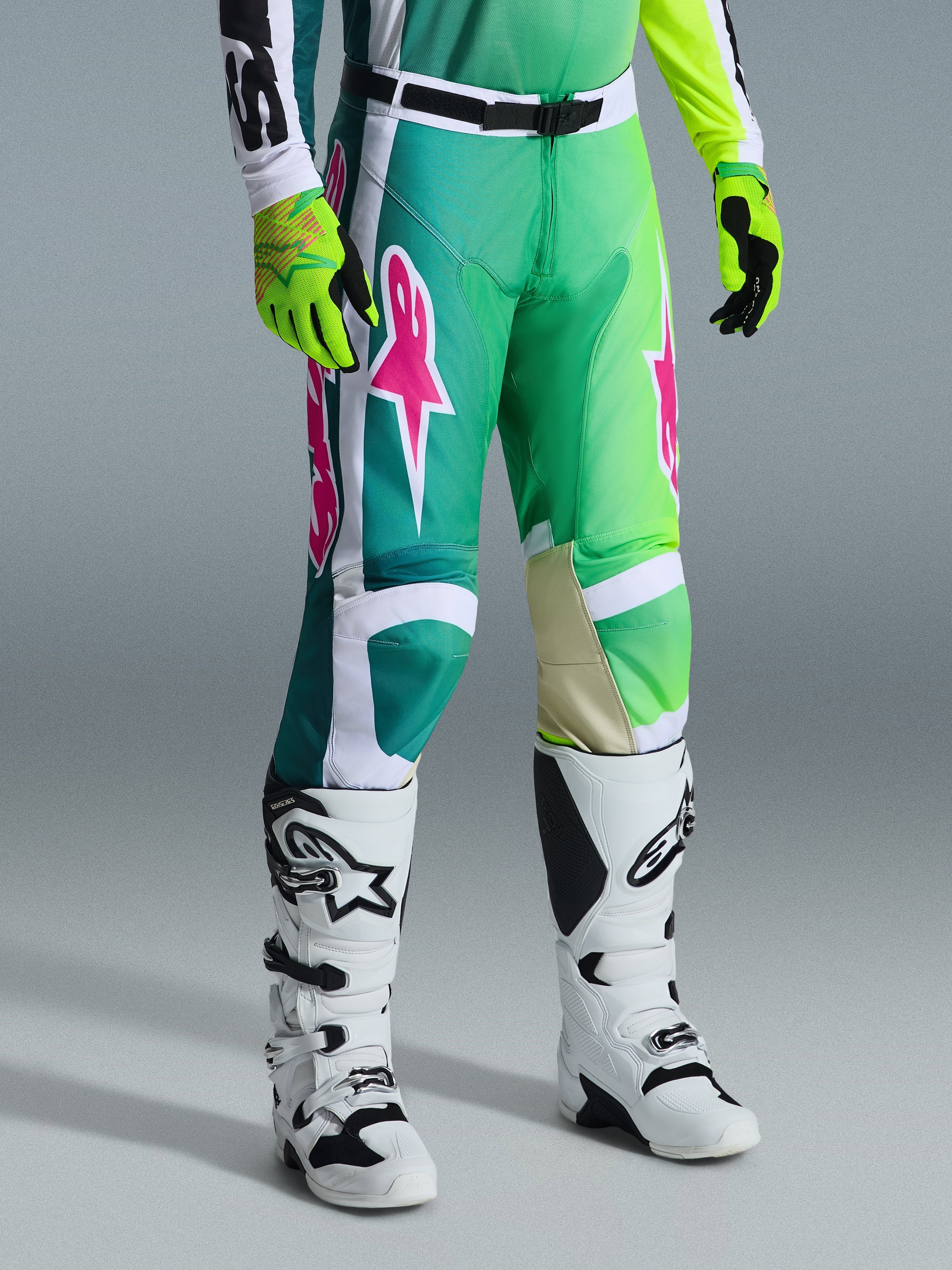 Alpinestars 2026 Racer Portl Hose, Motocross-Hose, Grün, Weiß und Schwarz mit pinkfarbenen Logos, kombiniert mit weißen Stiefeln und neongelben Handschuhen, mit auffälligen Grafikmustern und einer verstellbaren schwarzen Taillenschnalle, Performance-Ausrüstung für den Offroad-Sport