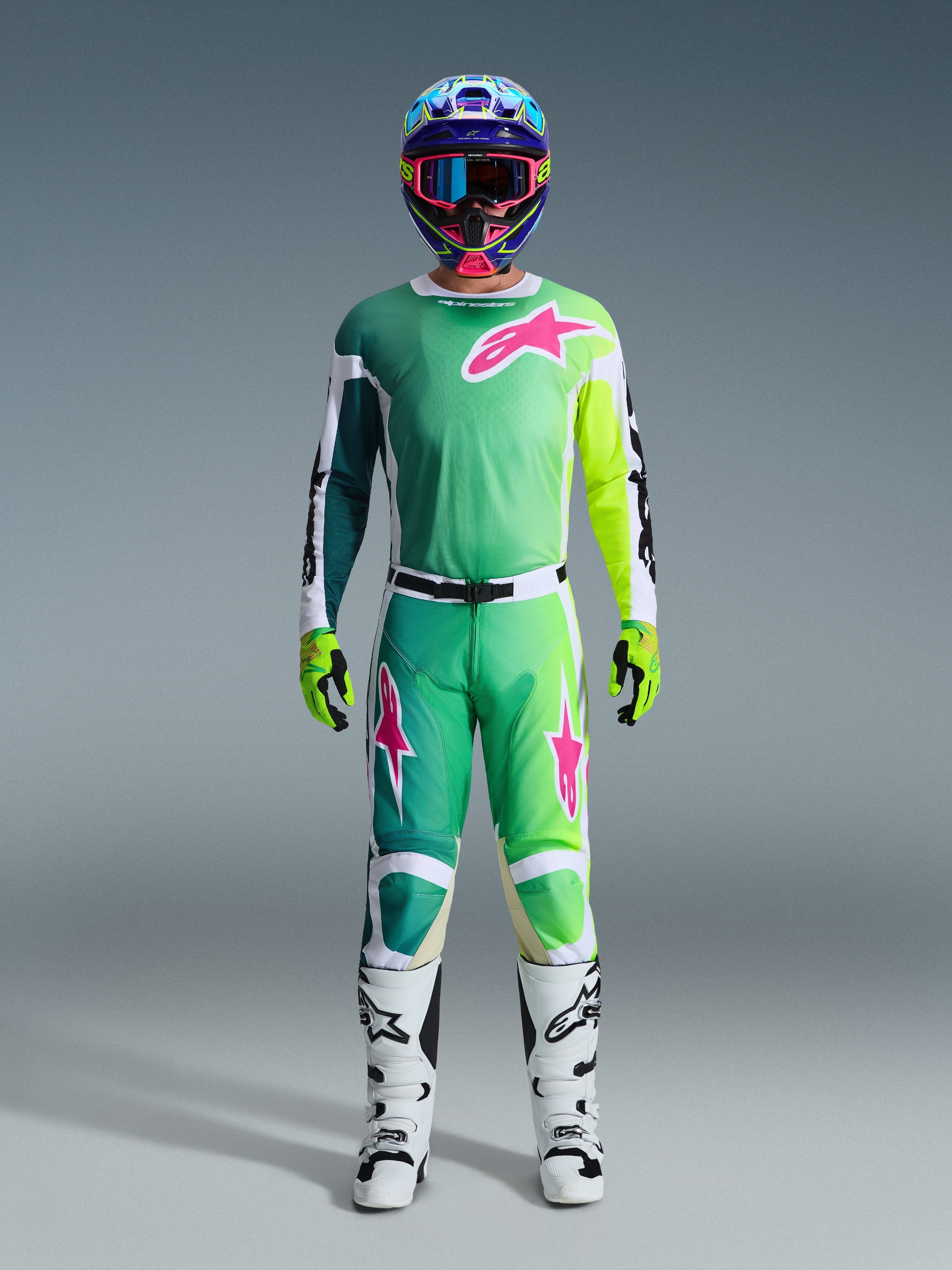 Alpinestars 2026 Racer Portl Gear Set, Motocross-Fahrer in kompletter Rennausrüstung, grünes Jersey und Hose mit pinken und weißen Grafiken, blauer mehrfarbiger Helm, weiß-schwarze Stiefel und grüne Handschuhe, abgestimmtes Outfit für den Offroad-Rennsport