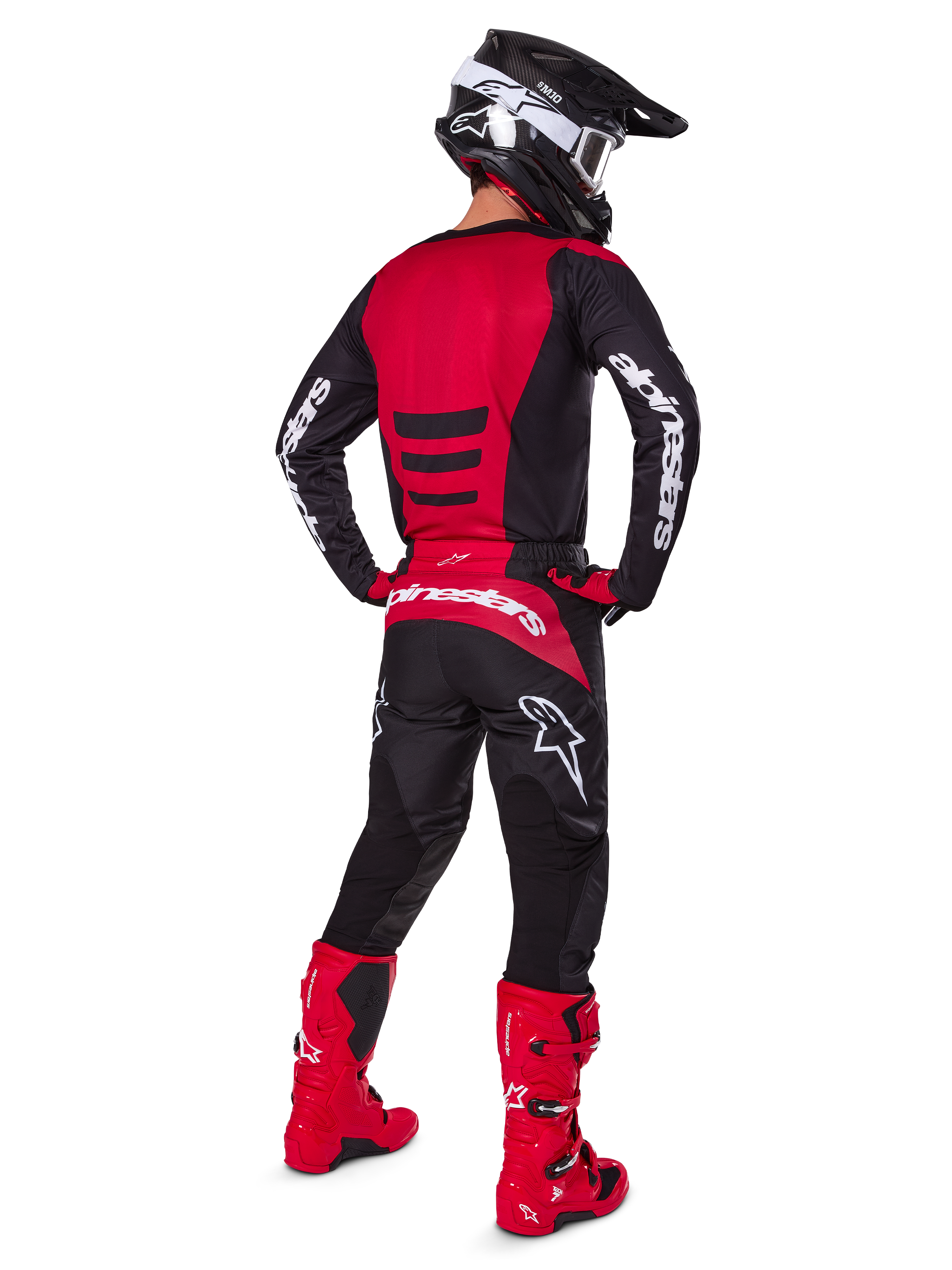 Motocross-Fahrer, der das Alpinestars 2025 Fluid Haul Gear Set in der Rückansicht trägt, rot-schwarzes Jersey mit weißem Branding, passende schwarze Hose mit roten Akzenten, leuchtend rote Stiefel und schwarzer Helm mit weißer Brille, komplett aufeinander abgestimmtes Outfit für Offroad-Rennen
