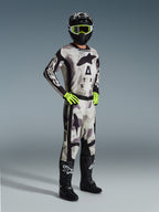 Motocross-Fahrer im 2026 Racer Lahnd Trikot in Sand Camo, grau-schwarzes Camouflage-Muster mit Alpinestars-Branding, passende Motocross-Hose, neongelbe Handschuhe, schwarzer Helm mit gelber Brille und schwarze Stiefel, komplette professionelle Offroad-Rennausrüstung.