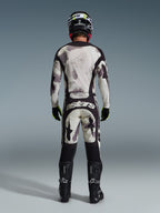 Motocross-Fahrer von hinten im 2026 Racer Lahnd Trikot und der passenden Hose in Sand Camo, mit einem abstrakten Muster in Creme und Grau sowie schwarzen Einsätzen, „astars“-Branding auf der Hose, kombiniert mit schwarzen Alpinestars-Stiefeln und einem schwarzen Helm für einen kompletten Offroad-Rennlook.