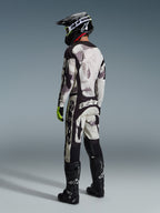 Motocross-Fahrer in kompletter Rennausrüstung, 2026 Racer Lahnd Trikot und passende Hose in Sand Camo, mit grau-schwarzem Camouflage-Muster und markanten Alpinestars-Logos, schwarzer Helm, schwarze Stiefel und neongelbe Handschuhe, Rückansicht.