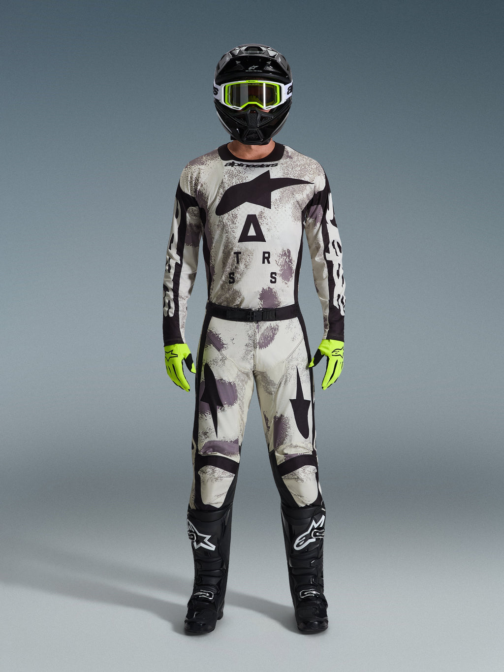 Motocross-Fahrer im Alpinestars 2026 Racer Lahnd Gear Set, Anzug mit Sand-Camo-Muster in Weiß, Grau und Schwarz, schwarzer Helm mit neongrüner Brille, leuchtend neongrüne Handschuhe und schwarze Stiefel mit weißen Logos, komplettes koordiniertes Outfit für den Offroad-Rennsport