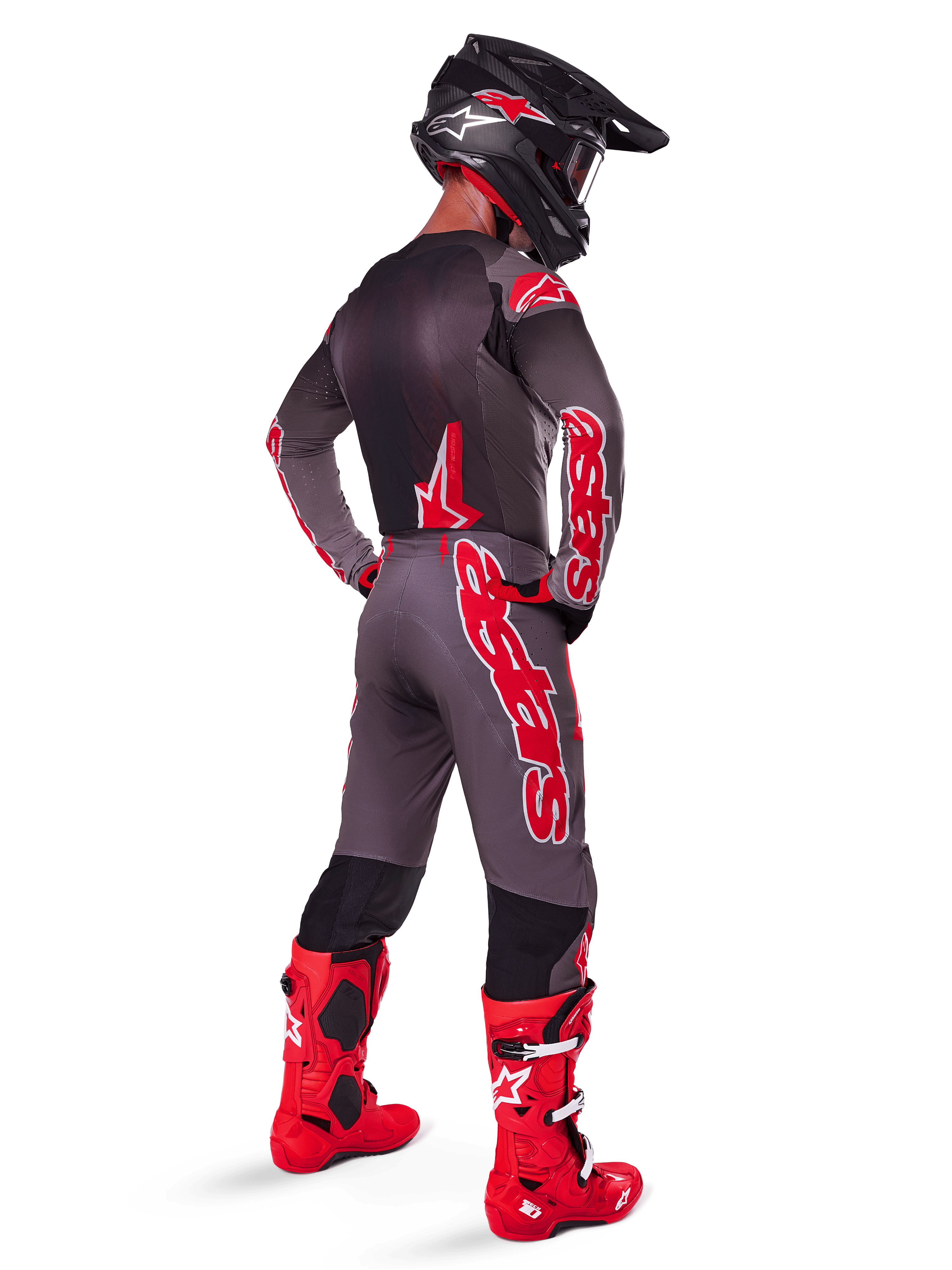 Motocross rider wearing Alpinestars 2025 Supertech Lipan Pants, Smoke Bright Red, grey pants with large red logos and black inner leg panels, paired with matching grey jersey, black helmet, and bright red boots, complete off-road racing outfit shown from the back.