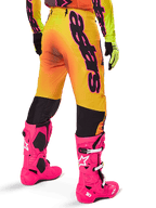 Alpinestars 2025 Supertech Lipan Ausrüstungsset, Rückansicht einer Motocross-Hose mit gelb-orangem Farbverlauf und markantem schwarzem Branding, kombiniert mit leuchtend pinken Tech 10 Stiefeln und gelben Handschuhen, professionelle Offroad-Rennausrüstung