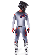 Motocross rider wearing Alpinestars 2025 Supertech Lipan Pants and matching jersey in Gray Orange Fluo, featuring bold orange and navy logos, paired with a black helmet, red gloves, and white and black boots, full racing kit for off-road performance.