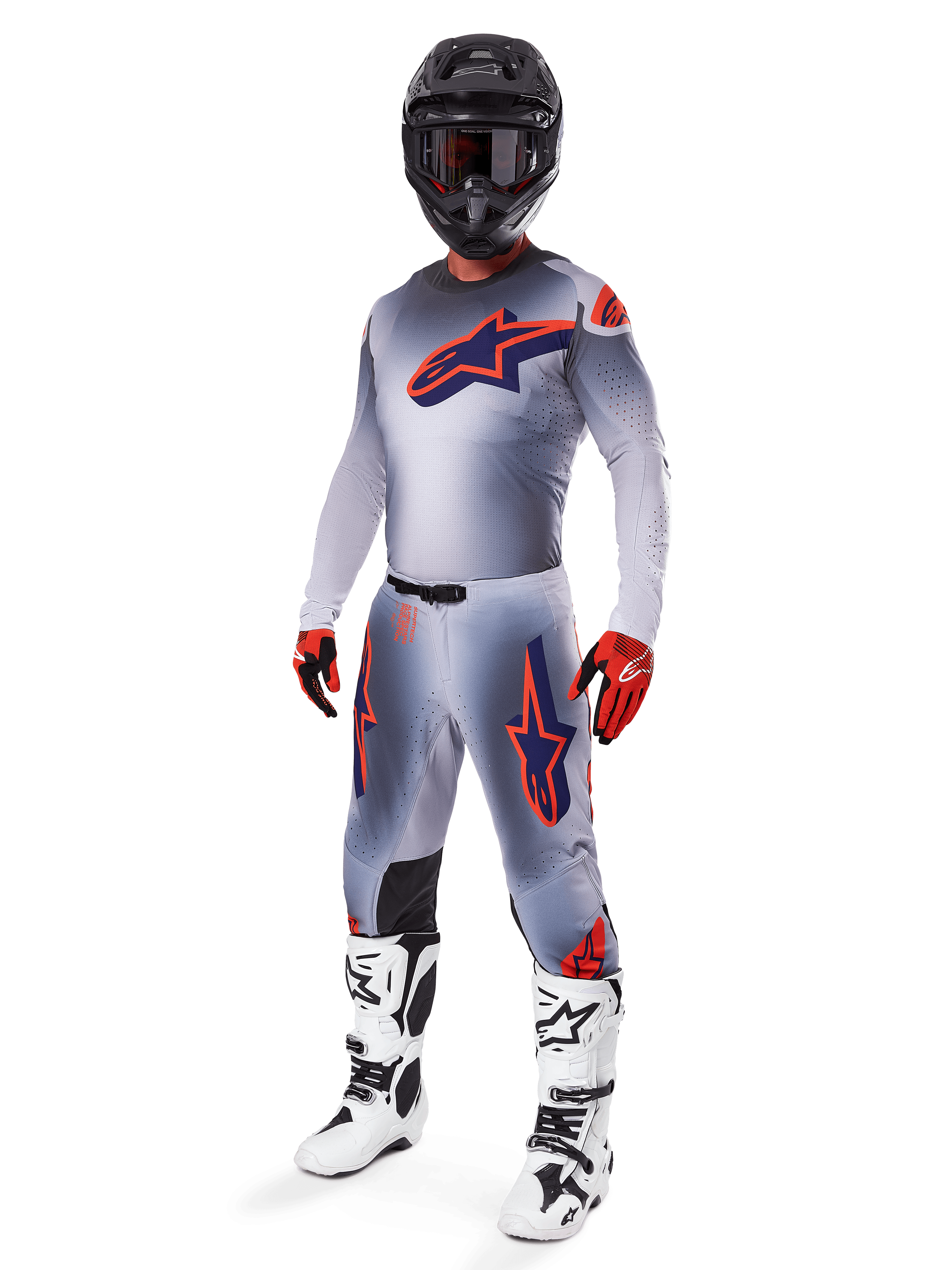 Motocross rider wearing full Alpinestars 2025 Supertech Lipan racing gear set, Gray and Orange Fluo, gray jersey with large orange chest logo, matching pants with orange accents, black helmet, red gloves, and white boots, professional off-road racing outfit