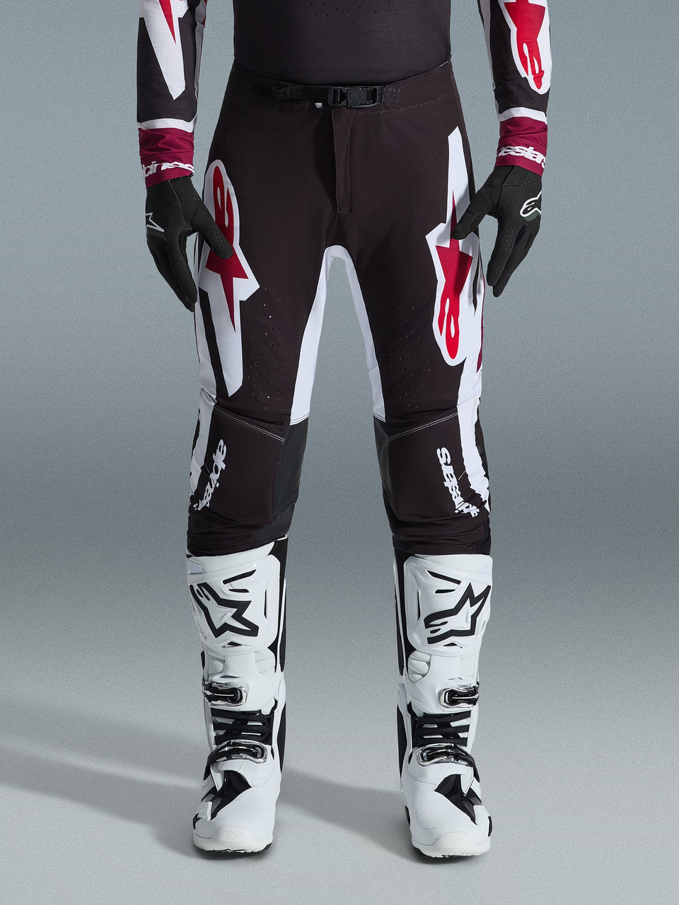 Alpinestars 2026 Supertech AFD Vista Hose, Motocross-Hose, Schwarz, Rot und Weiß, mit großen Grafik-Logos auf den Oberschenkeln und Knien, kombiniert mit weißen Rennstiefeln und schwarzen Handschuhen, athletisches, rennbereites Design für den Elite-Offroad-Wettbewerb