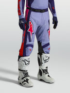 Alpinestars Racer Air Hunt Hose, belüftete Motocross-Ausrüstung in Lila und Pink, am Modell mit weißen Stiefeln.