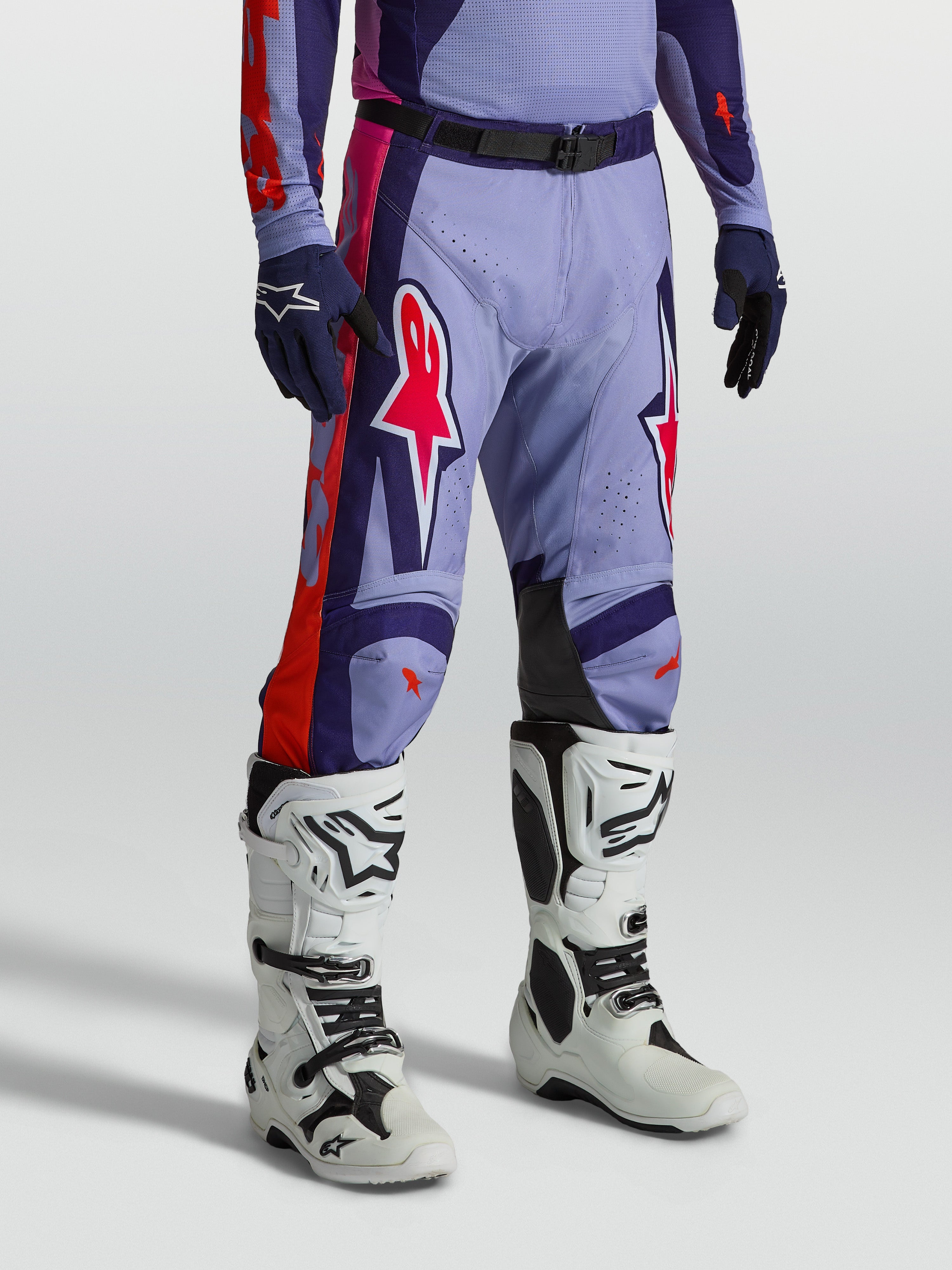 Alpinestars Racer Air Hunt Hose, belüftete Motocross-Ausrüstung in Lila und Pink, am Modell mit weißen Stiefeln.