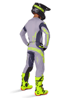 Motocross-Fahrer von hinten gesehen in kompletter Rennausrüstung, Alpinestars 2025 Techstar Dreem Hose in Grau und Dunkelgrau mit auffälligen neongelben Akzenten, passendes graues Trikot mit Neon-Grafiken, leuchtend neongelbe Stiefel und schwarzer Helm, professionell abgestimmtes Motocross-Outfit