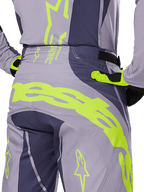 Alpinestars 2025 Techstar Dreem Hose, Motocross-Hose, Grau und Dunkelgrau mit neongelben Akzenten, Rückansicht mit markantem Alpinestars-Branding auf der Passe, getragen mit passendem Trikot und Handschuhen, entwickelt für den Offroad-Rennsport.
