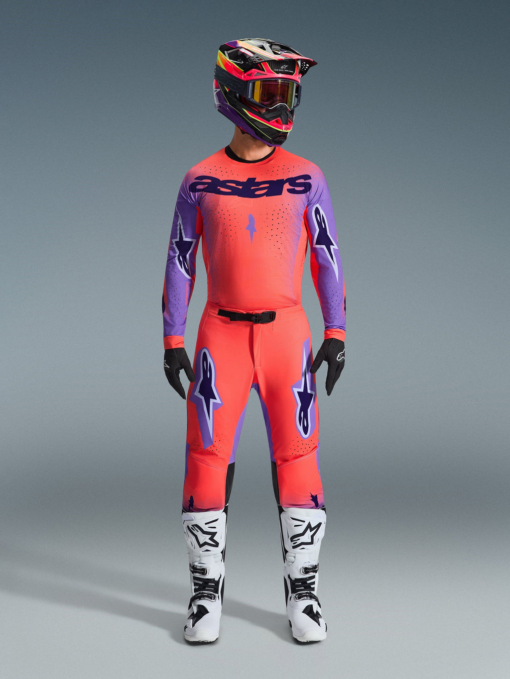 Alpinestars 2026 Supertech Scenz Hose, Motocross-Hose, Hot Coral und Lila, getragen als komplettes Gear-Set mit passendem Trikot und Helm, weiße und schwarze Stiefel, mit lila Logos und athletischer Race-Passform.