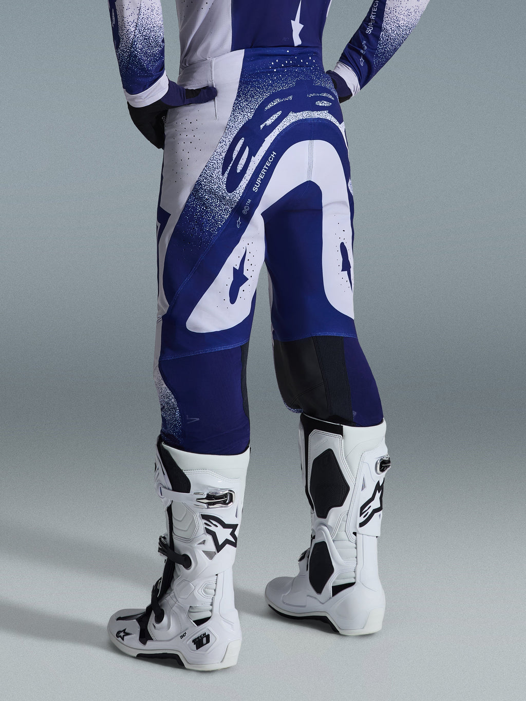 Alpinestars 2026 Supertech Scenz Pants, Motocross Pants, Light Gray and Dark Blue, rear view worn with matching jersey and white boots, featuring bold blue graphics with speckled accents, performance athletic fit for off-road racing.