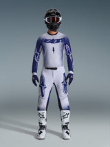 Motocross-Fahrer im Alpinestars 2026 Supertech Scenz Gear Set, Hellgrau und Dunkelblau, inklusive Trikot und Hose mit passenden blauen Handschuhen, weiß-schwarzen Stiefeln und einem schwarzen Helm mit weißer Brille, koordiniertes Outfit für professionellen Offroad-Rennsport