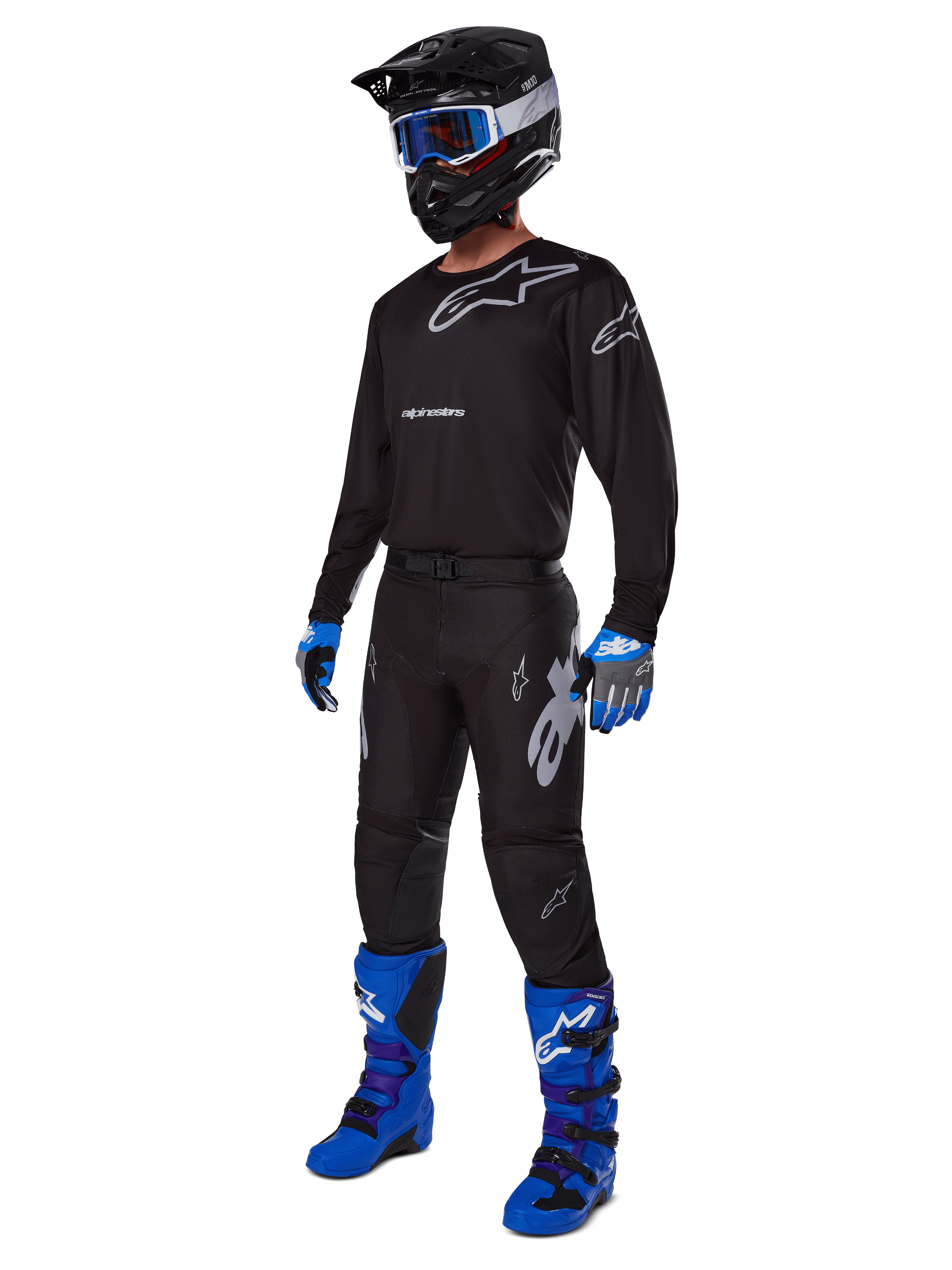 Motocross rider wearing complete Alpinestars racing gear, 2025 Racer Graphite Pants in Black and Gray, matching black jersey with grey logos, black helmet with blue goggles, bright blue and purple boots, and blue and grey gloves, coordinated outfit for off-road racing