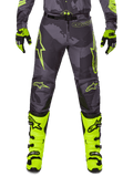 Alpinestars 2025 Racer Hollow Hose, Motocross-Hose, Dunkelgrau mit Neongelb, Sterndesigns und Logo, Person trägt komplette Offroad-Schutzausrüstung mit schwarzen und neongelben Handschuhen und neongelben Stiefeln