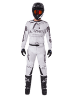 Motocross-Fahrer in der Alpinestars 2025 Racer Hollow Hose in Light Camo Brown, kombiniert mit einem passenden weiß-grauen Langarm-Trikot, schwarzem Helm mit orange-roter Brille, schwarzen Handschuhen und schwarzen Stiefeln, abgestimmtes Rennbekleidungs-Set für Offroad-Performance.