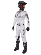 Alpinestars 2025 Racer Hollow Hose, Motocross-Hose, Light Camo Brown, gezeigt als Teil einer kompletten Rennausrüstung mit weißem Trikot, schwarzem Helm und schwarzen Stiefeln, mit verstärkten schwarzen Kniepaneelen und einem dezenten Camouflage-Design.