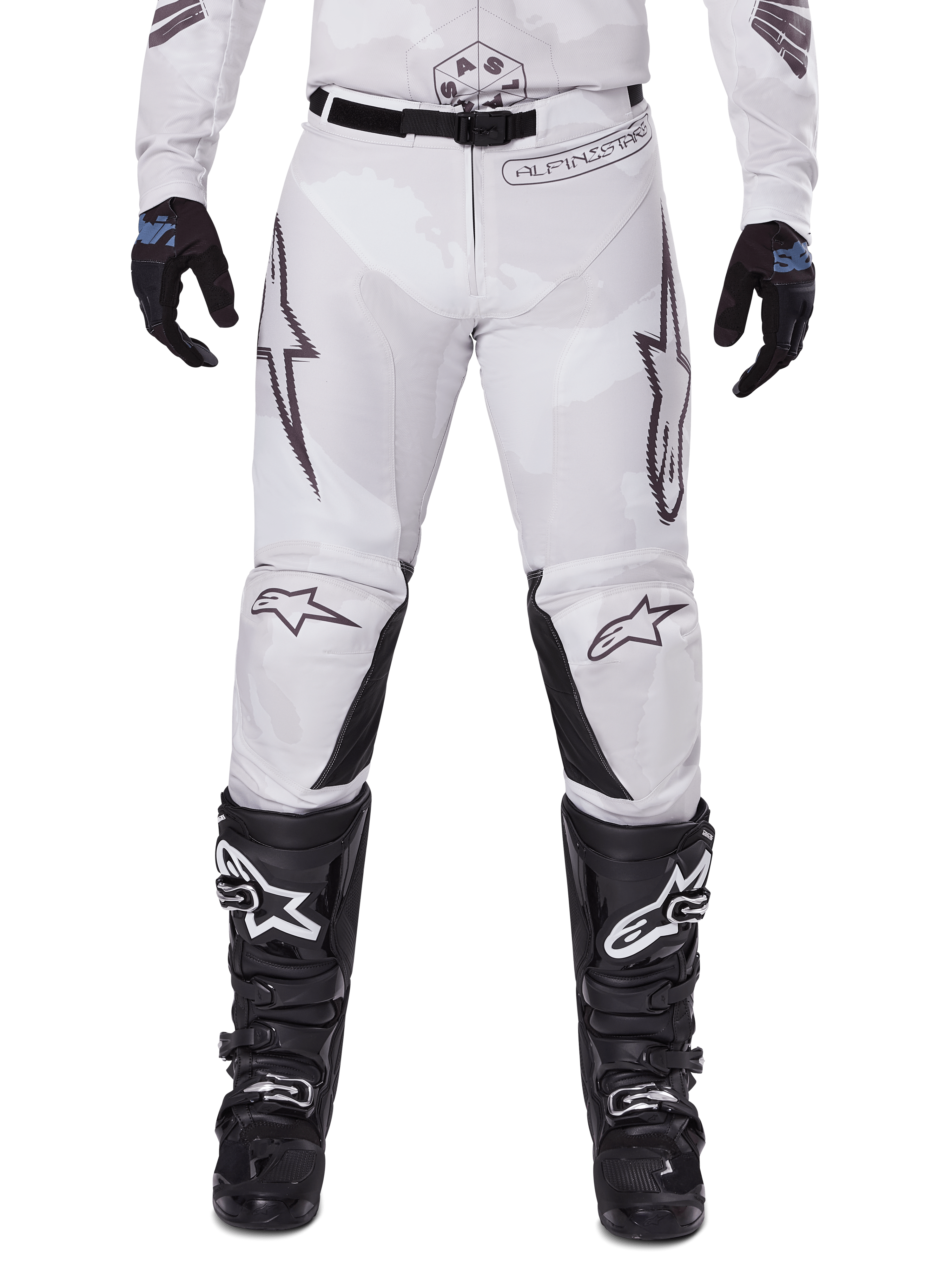 Alpinestars 2025 Racer Hollow Hose, Motocross-Hose, Light Camo Brown, getragen mit schwarzen Handschuhen und Motocross-Stiefeln, mit dezentem Camouflage-Muster, schwarzen Grafikdrucken und Astars-Logos, ergonomisches Design für Performance-Offroad-Fahrten