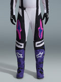 Alpinestars 2026 Techstar Knif Hose, Motocross-Hose, Schwarz, Weiß und Lila mit pinkfarbenen und blauen Akzenten, getragen mit lila Rennstiefeln und schwarzen Handschuhen, verfügt über einen ergonomischen Rennschnitt und markante Logo-Grafiken für Offroad-Performance