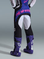 Alpinestars 2026 Techstar Knif Hose, Motocross-Hose, Schwarz, Hellgrau und Lila, Rückansicht mit pinkem Branding auf dem Gesäß, getragen mit passendem Trikot und lila Motocross-Stiefeln, professionelles Offroad-Rennoutfit