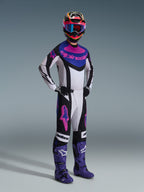 Motocross-Fahrer im Alpinestars 2026 Techstar Knif Gear Set, Schwarz, Hellgrau und Lila, weißes Trikot mit blauen und rosa Akzenten, passende Hose mit lila Stern-Logos, farbenfroher pinker und gelber Helm, lila Motocross-Stiefel und schwarze Handschuhe, professionelle Ausrüstung für den Offroad-Rennsport.