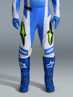 Alpinestars 2026 Techstar Knif Hose, Motocross-Hose, UCLA Blau, Schwarz und Fluo-Gelb, kombiniert mit passenden blauen Handschuhen und Stiefeln, mit weißen Einsätzen und leuchtenden gelben Fluo-Logos, ergonomische Racing-Passform für Offroad-Performance
