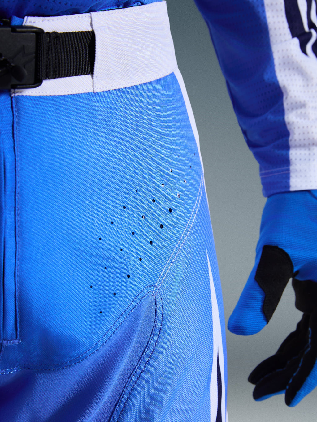 Alpinestars 2026 Techstar Knif Hose, Ucla Blau und Weiß, Nahaufnahme des Hüftbereichs mit lasergeschnittenen Perforationen zur Belüftung, SX2-Magnetverschluss am Bund und passenden Motocross-Handschuhen