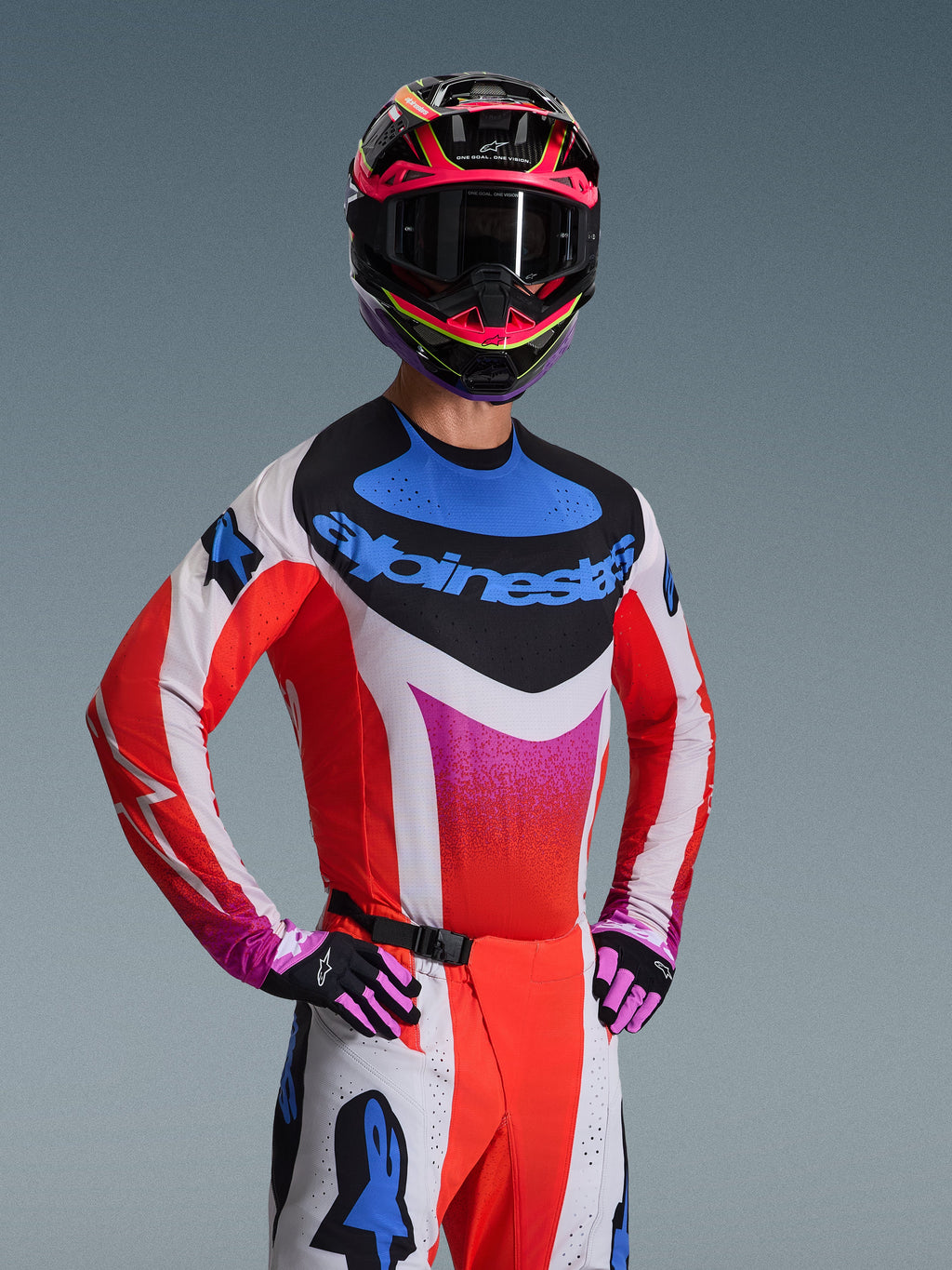 Alpinestars 2026 Techstar Knif Trikot, Motocross-Trikot, Weiß mit roten, blauen und pinkfarbenen Farbverlaufsmustern, mit markantem blauem Branding auf der Brust, getragen mit abgestimmtem Helm und Handschuhen, athletisches Rennsportdesign für Offroad-Performance
