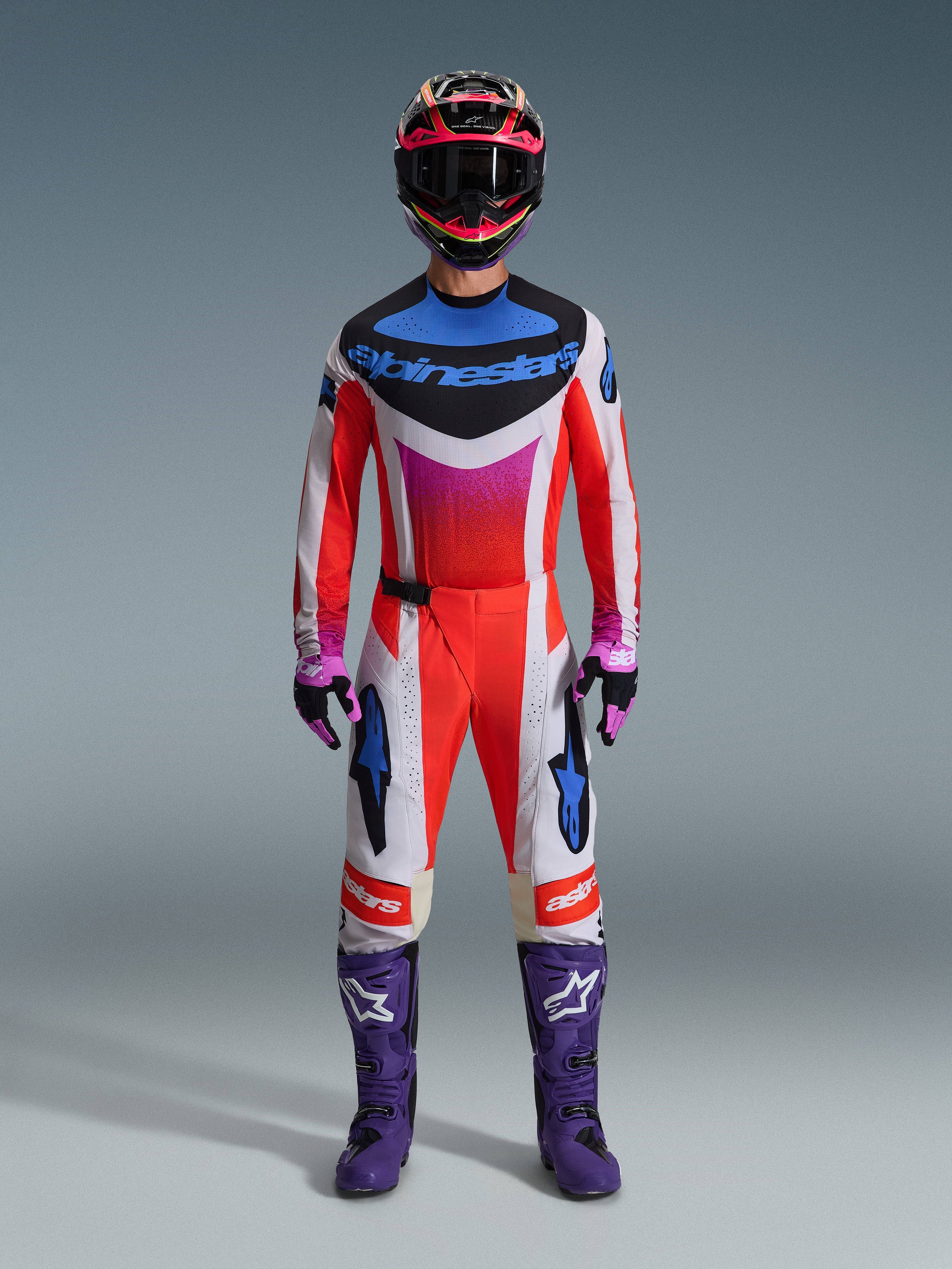Motocross rider wearing the 2026 Techstar Knif Gear Set, complete racing outfit in red, white, and black with blue branding and pink accents, featuring purple boots with white logos, pink and black gloves, and a black and pink helmet, professional off-road racing gear