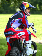 Motocross-Fahrer auf einem roten Dirtbike, trägt Alpinestars 2025 Fluid Wurx Hose in Lila und leuchtendem Rot, passendes Trikot, weiß-schwarze Tech 10 Stiefel, weiße Handschuhe und Red Bull Helm, komplette Offroad-Rennausrüstung im Freien