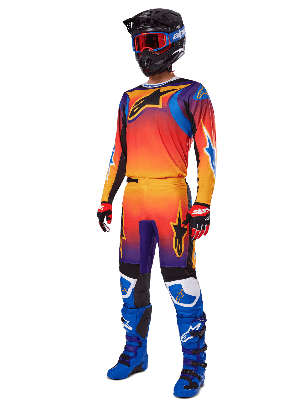 Motocross rider wearing complete racing gear, Alpinestars 2025 Fluid Wurx Pants and matching jersey in a multicolor orange, red, and purple gradient, black helmet with red goggles, blue and black boots, red and black gloves, coordinated outfit for off-road racing