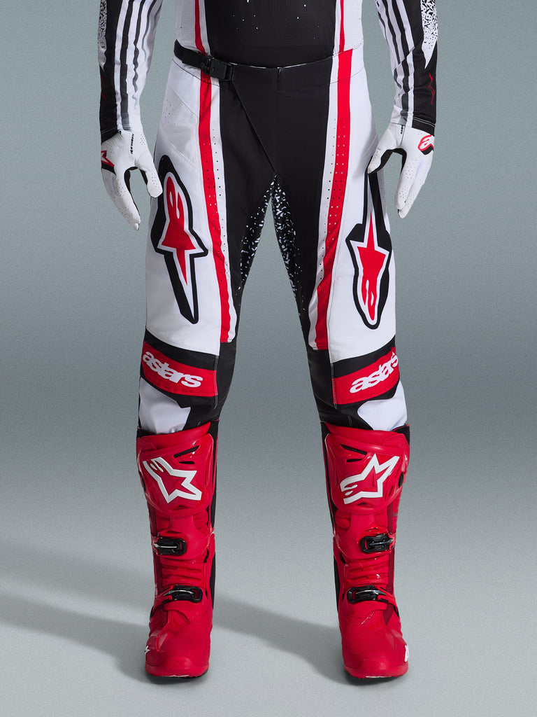 Alpinestars 2026 Techstar Nomur Pants, Motocross Pants, Black White and Red, worn with matching red boots and white gloves, featuring bold red logos on the thighs and 'astars' branding on the knees, multi-panel racing design for off-road performance