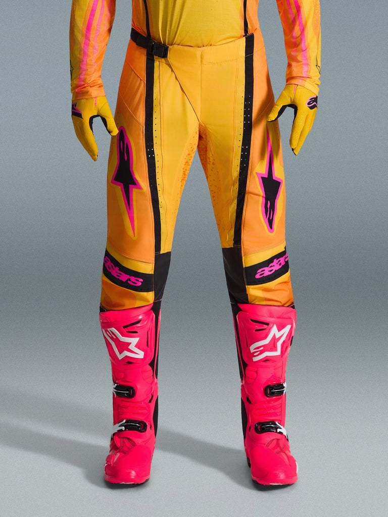 Alpinestars 2026 Techstar Nomur Pants, Motocross Pants, Orange Yellow and Pink, worn with matching yellow gloves and bright pink racing boots, featuring black panels and bold pink Alpinestars branding, technical off-road racing gear