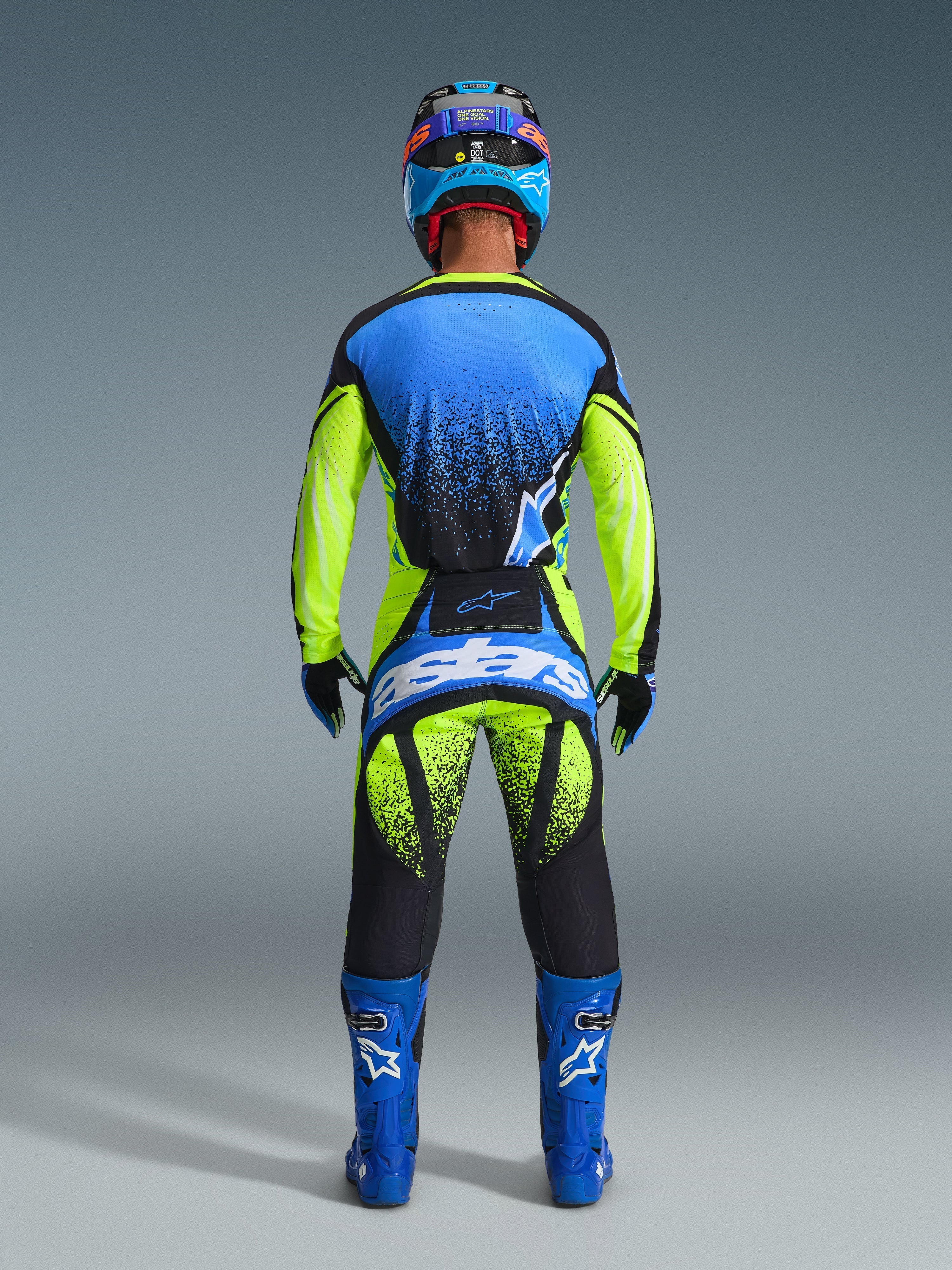 Motocross-Fahrer in der Rückansicht, Alpinestars 2026 Techstar Nomur Hose in Gelb Fluo und UCLA Blue mit dunkelblauen Akzenten, passendes Trikot und blaue Stiefel, markantes Astars-Branding am Gesäß, gesprenkeltes Grafikdesign.