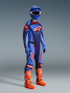 Alpinestars 2026 Techstar Nomur Hose, Motocross-Hose, Dunkelblau, Orange und UCLA-Blau, getragen von einem Fahrer in kompletter Rennausrüstung mit passendem Trikot, blauem Helm und leuchtend orangen Stiefeln, leistungsorientiert für Offroad-Rennsport entwickelt