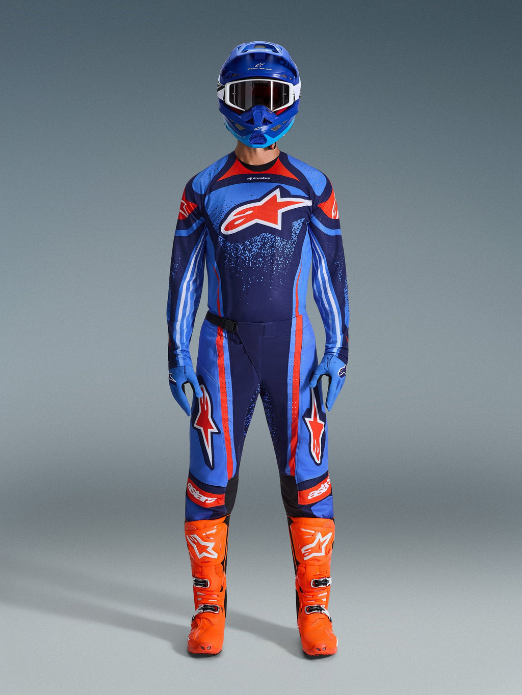 Alpinestars 2026 Techstar Nomur Gear-Set, Motocross-Fahrer in voller Rennausrüstung, Dunkelblau mit orangefarbenen und UCLA-blauen Akzenten, passendes Trikot und Hose mit großen Logos, blauer Helm und leuchtend orangefarbene Stiefel, abgestimmte Offroad-Wettkampfausrüstung.